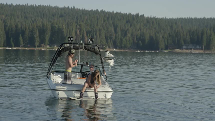 Three people are on a ski boat sitting on a lake