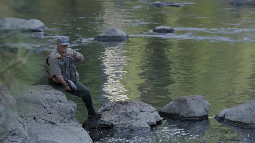 A fisherman holds a net with a fish next to a river