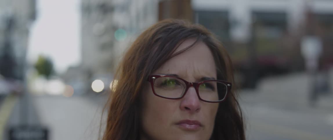 A serious woman in glasses walks in an urban setting
