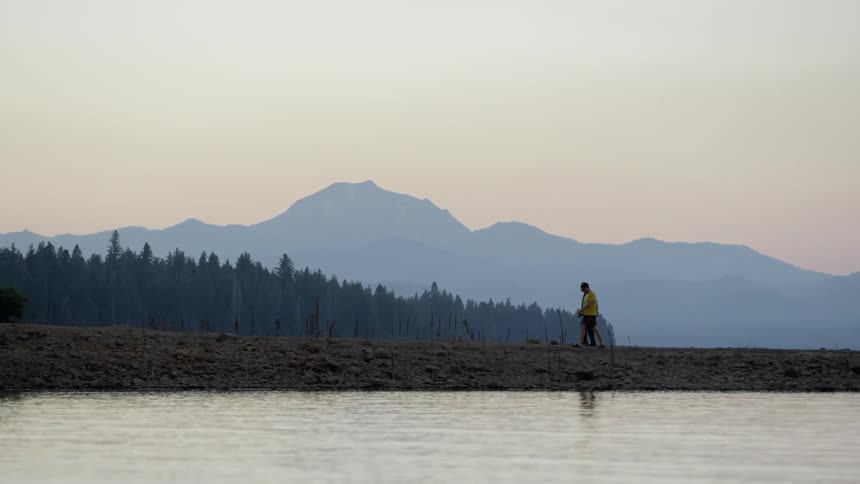 A view of mountains, trees, and some water in the foreground
