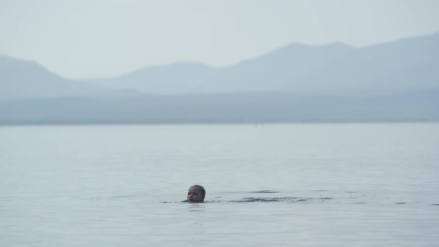 A child is swimming in the water with mountains in the back