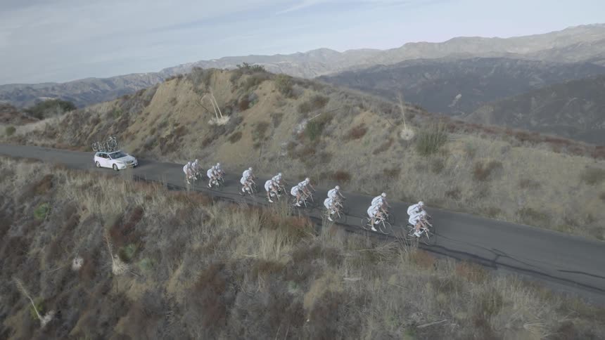 A group of bicyclists are riding on a mountain road with a car following them