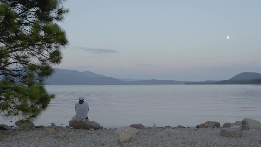 A person sits on a rock by the water