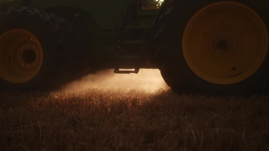 Farm tractor operating through a field with the sun on the horizon