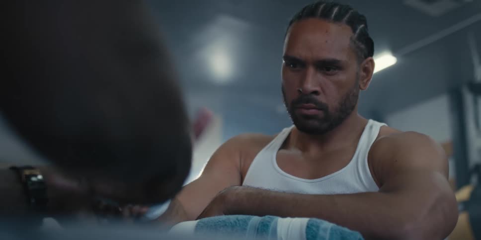 Boxer with serious expression while sitting and a man is putting a bandage between his fingers and wrist