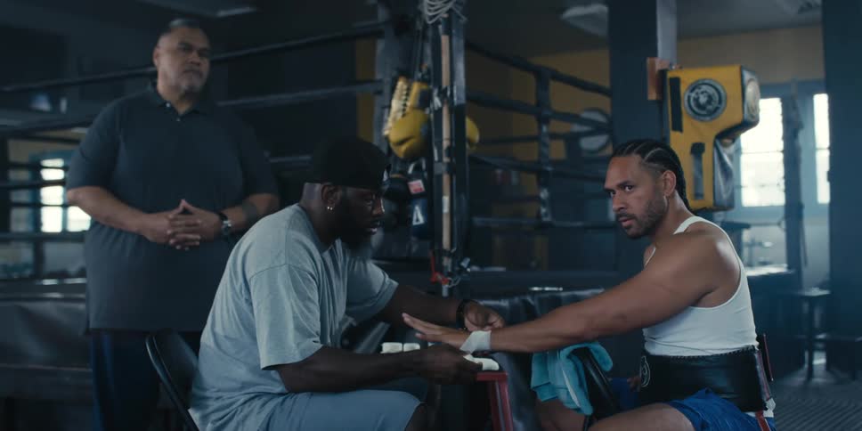 In a boxing gym a coach wraps the hands of a boxer sitting on a chair