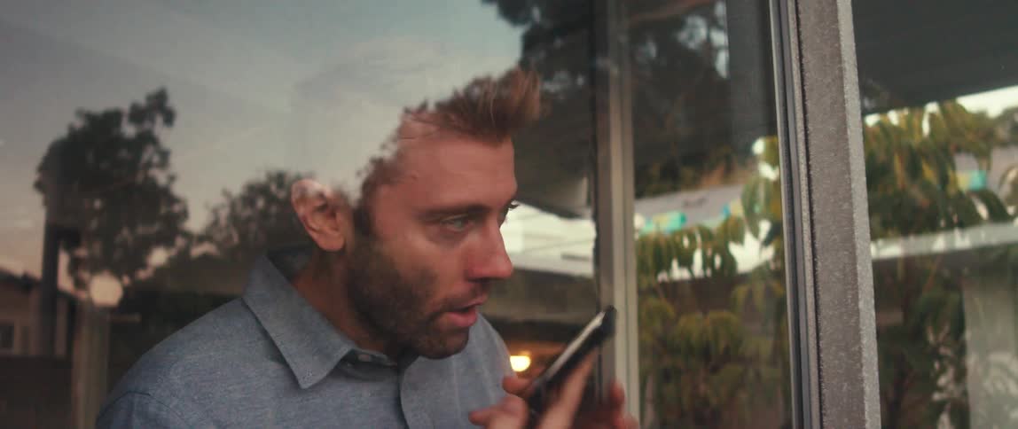 Close up of a man talking on a smartphone near a large window at home