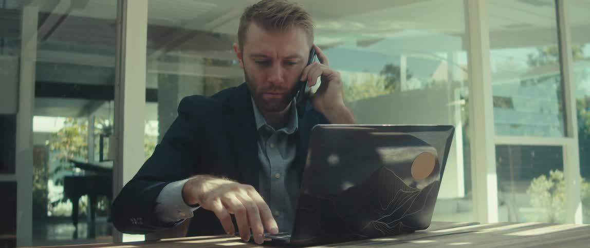 An image of a man working on a laptop and having a conversation on phone
