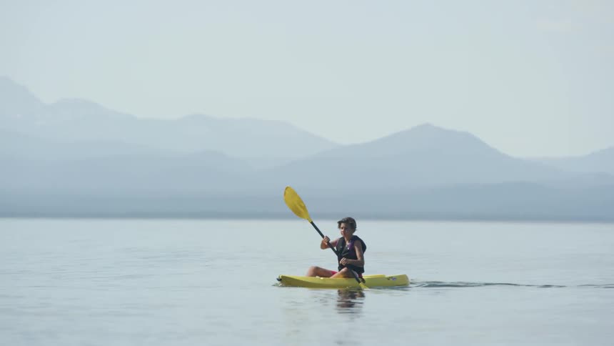 A person in a canoe rowing with mountains in the background