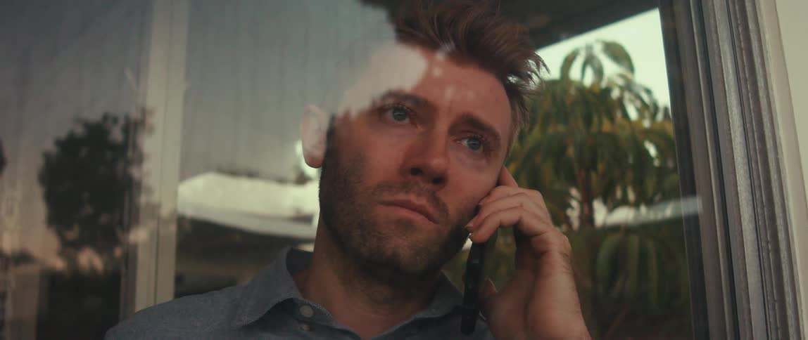 The face of a young man talking on a cell phone in front of a glass window reflecting the outside environment