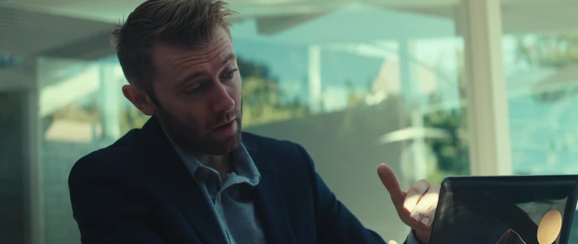 The face of a young man who is wearing a suit and talking to someone through the screen of his laptop which is in front of him