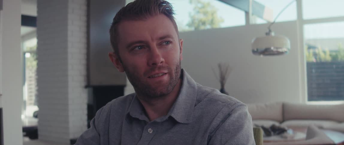 A man in a shirt works on a laptop in a welllit living room in a modern home