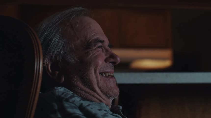 Side portrait of an elderly man sitting watching and laughing