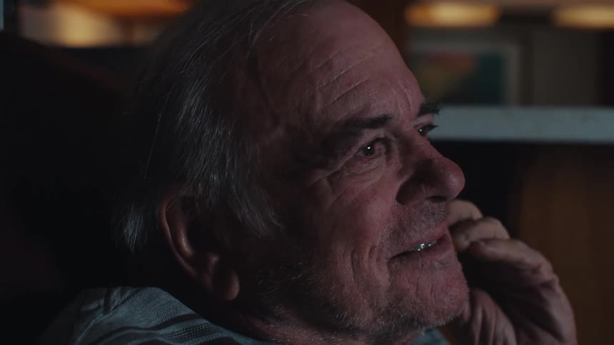 An older male is smiling as he looks forward in a dark room