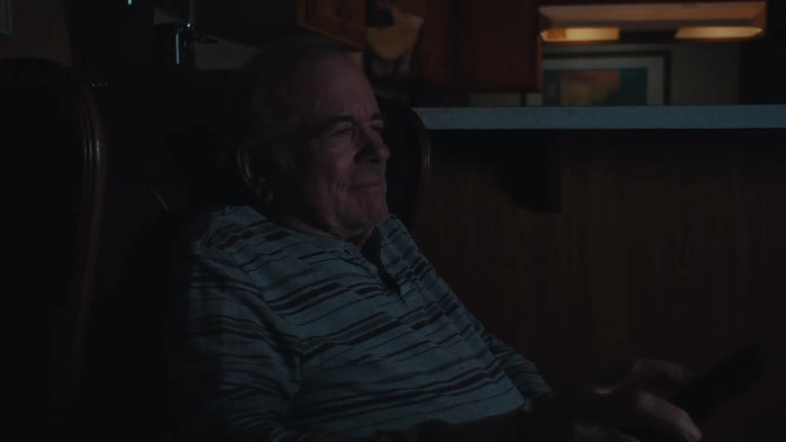 Elderly man sitting in an armchair watching television and using the remote control