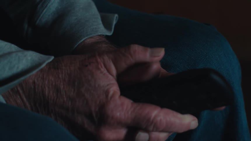 Elderly man sitting watching in a concentrated and apprehensive manner and holding the television remote control in his hands