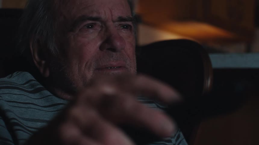 Elderly man sitting in an armchair and using a television remote control