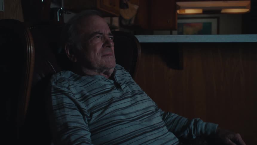 An elderly man sits at home watching television at night