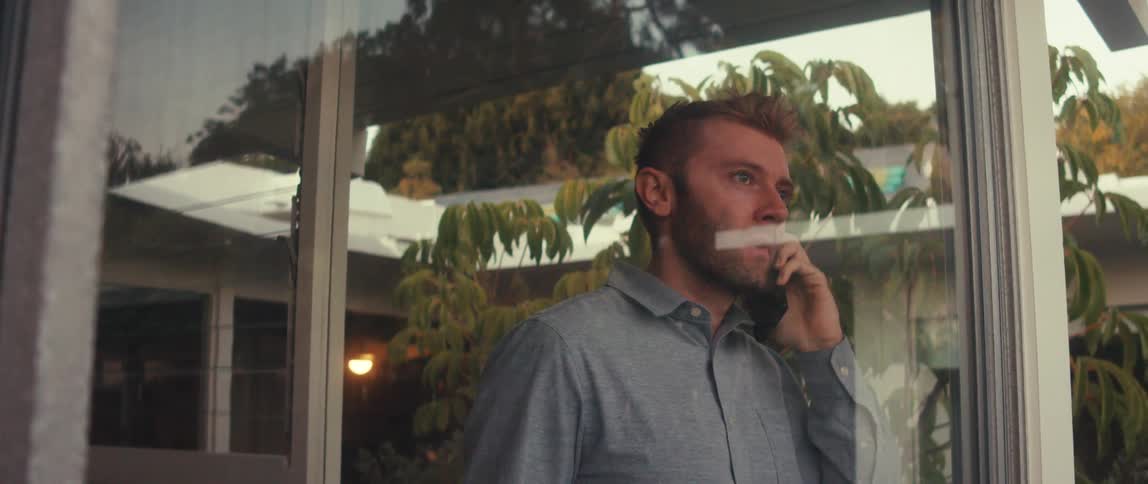 A man is walking near a glass window and when he is talking on the cell phone and he is surprised