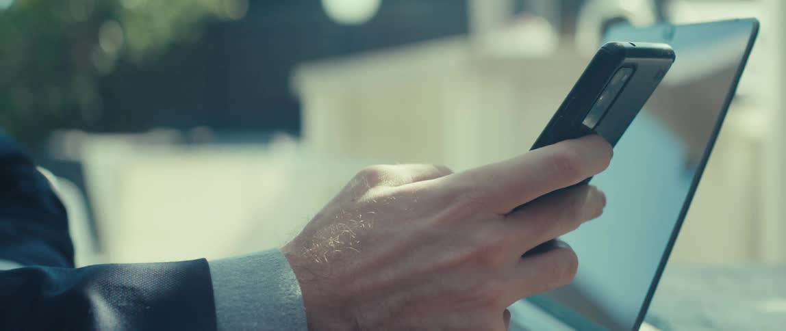 A man typing on a laptop then stopping to check his smart phone