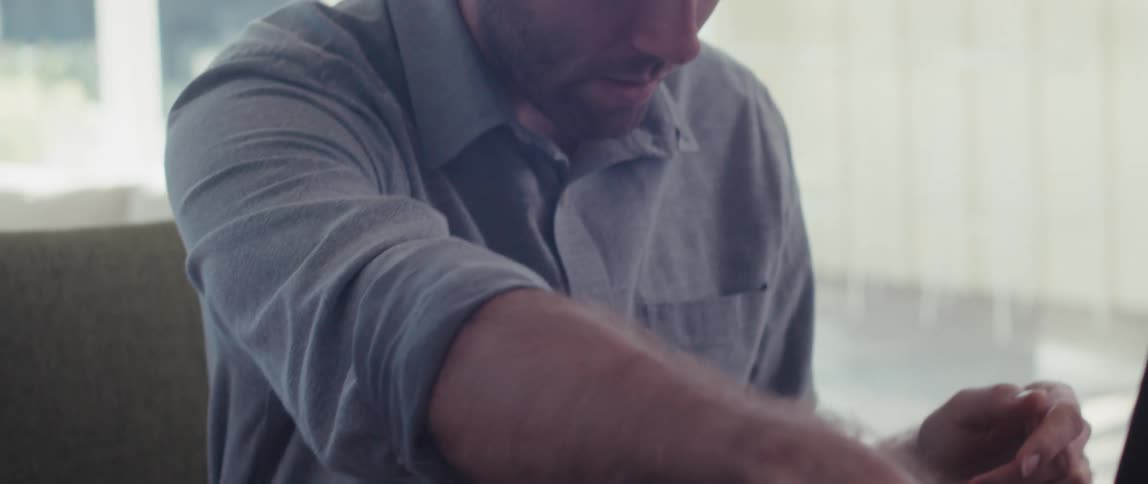 Seated man making hand gestures while in an online meeting in front of a laptop