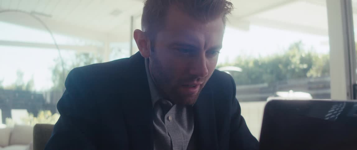Man in blazer sitting in front of laptop with his eye close to the screen