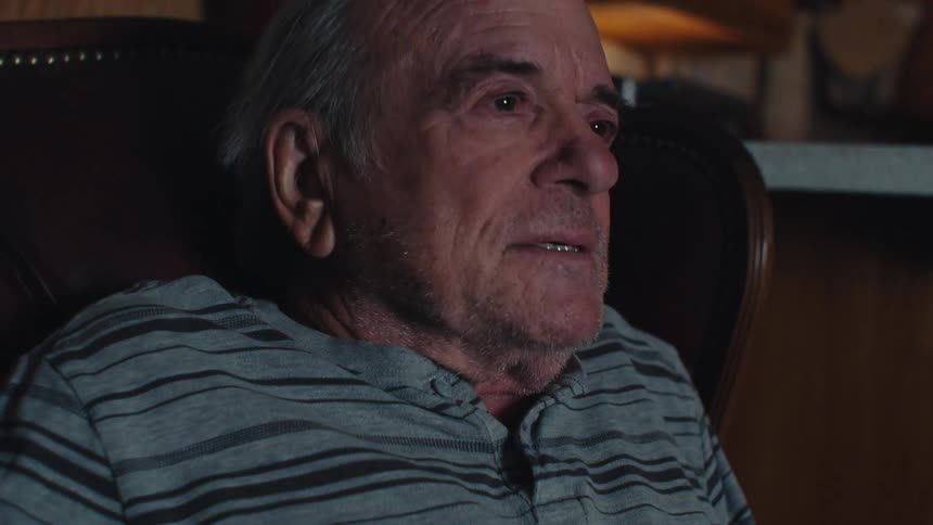 Elderly man sitting in an armchair in a dark room feeling emotional