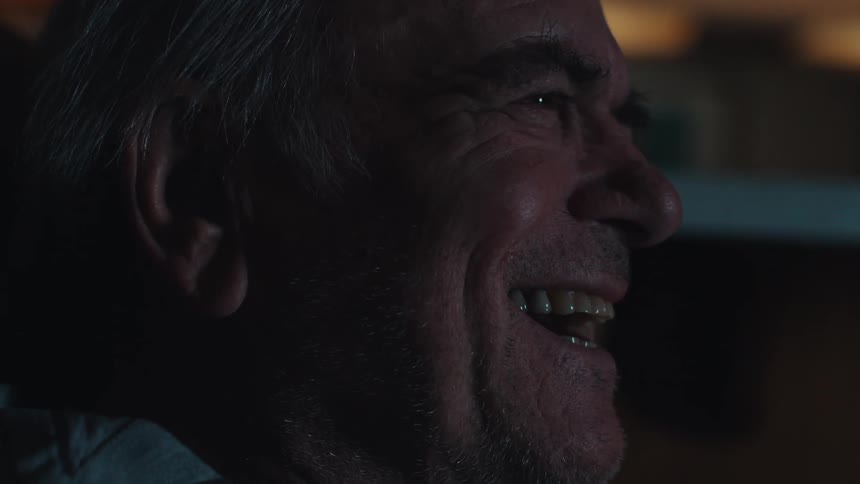 Portrait of an elderly man laughing out loud while sitting in a dark room