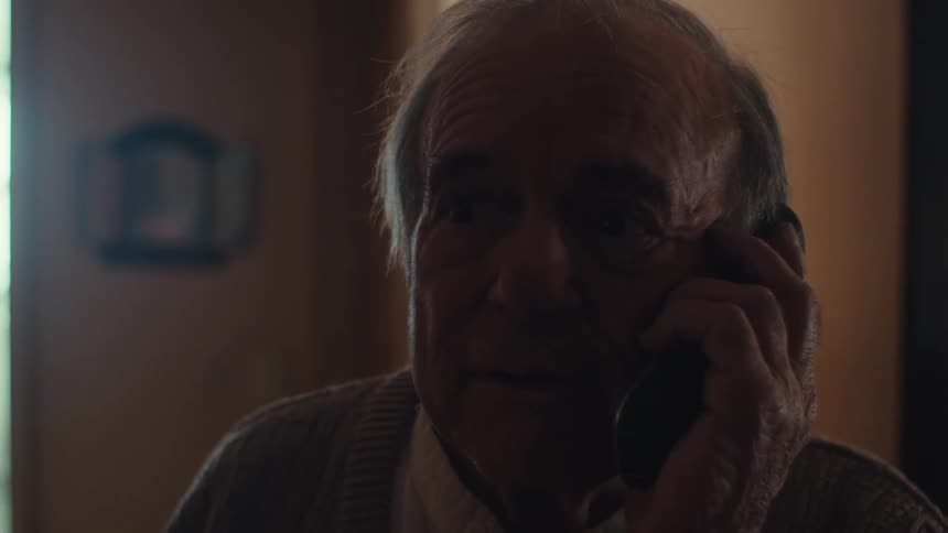 Elderly man smiles while talking on the phone at home