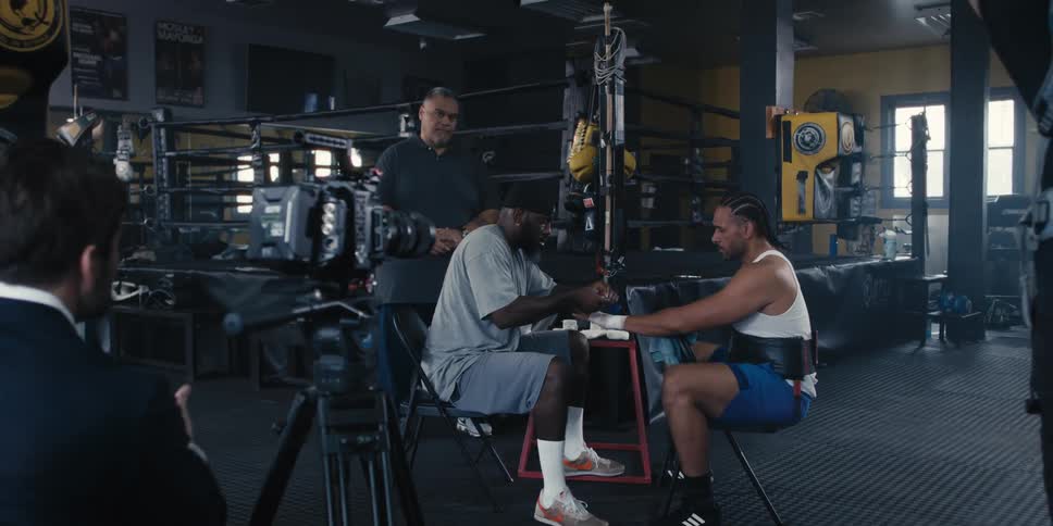 Camera filming a person bandaging a fighters hand next to a boxing ring