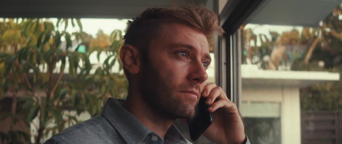 Close up of a man talking on a smartphone near a large window at home