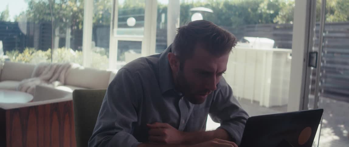 A man in a shirt works on a laptop in a welllit living room in a modern home