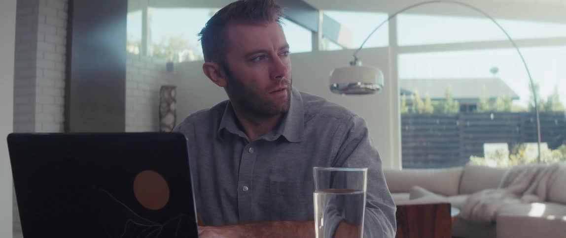 Man sitting at a table with a glass of water and typing on laptop