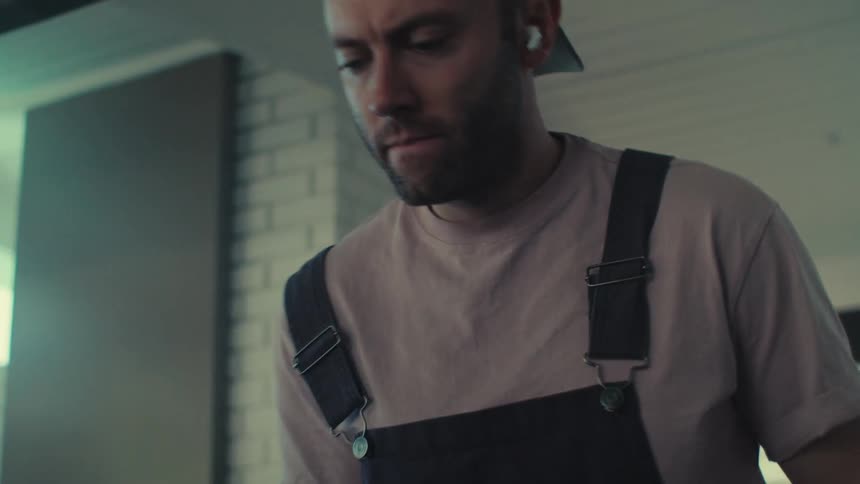 A man is working on something in a building nodding his head to the music