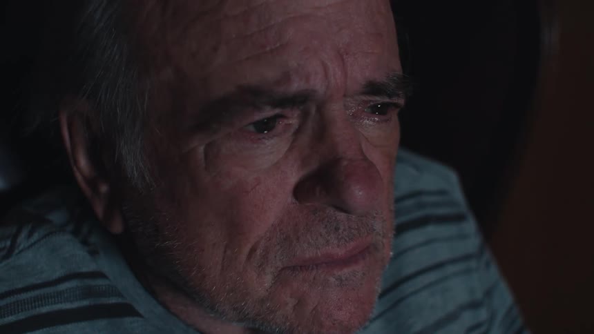 Closeup of a sad elderly man watching television in a dimly lit room