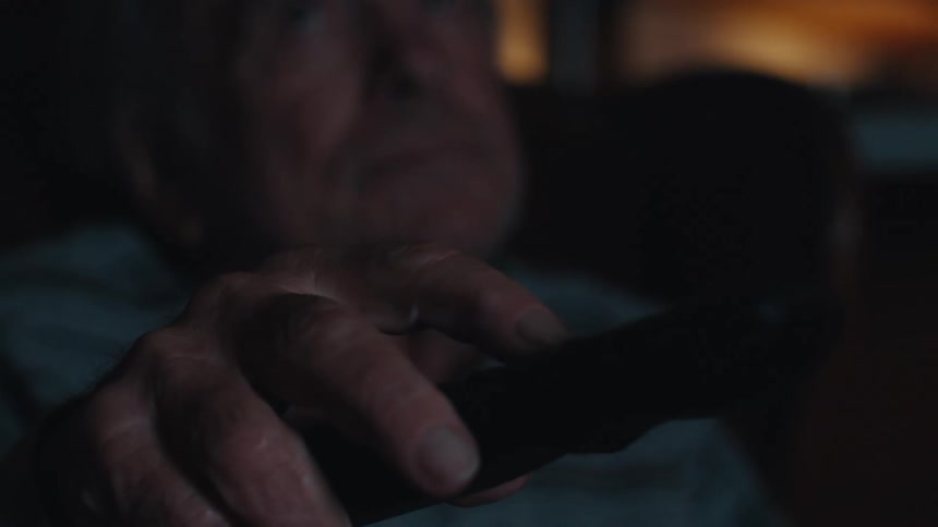 Close up of an elderly man watching tv holding a remote control