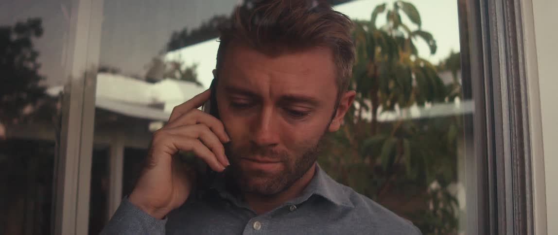 A man at a window looking sad as he talks on the phone