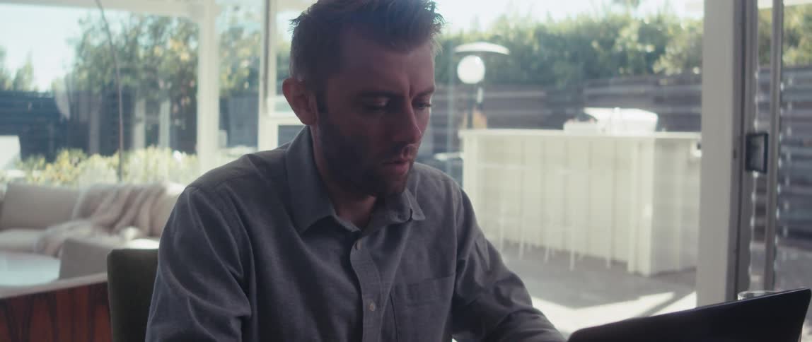 Close up of a man working on a laptop in a well lit living room near large windows