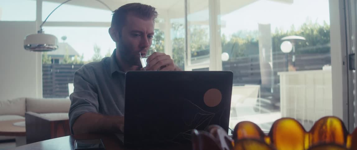 Man sitting drinking a glass of water and working in front of the laptop