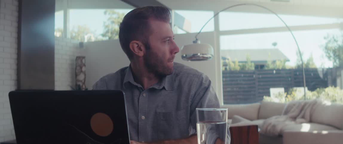 A man in a shirt works on a laptop in a welllit living room in a modern home