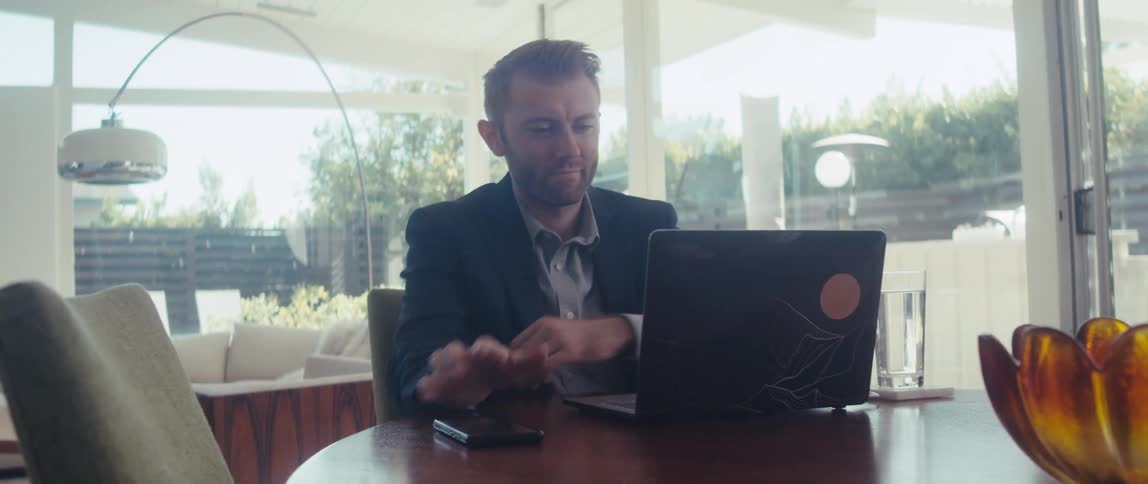 A man in a suit works on a laptop in a welllit living room in a modern home