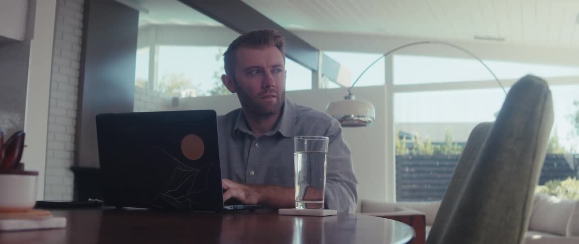 A man in a shirt works on a laptop in a welllit living room in a modern home