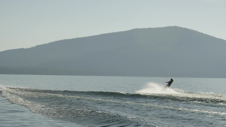 A woman wakeboards behind a boat on a lake
