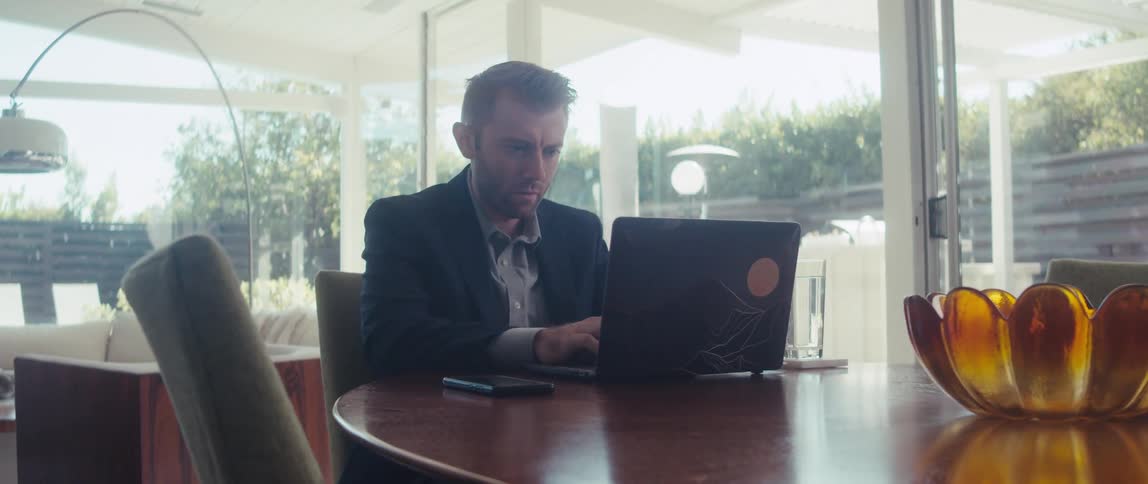 A man in a suit works on a laptop in a welllit living room in a modern home