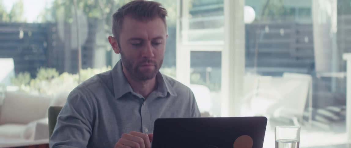 A man in a shirt works on a laptop in a welllit living room in a modern home