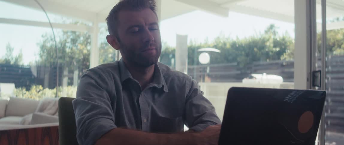 A man in a shirt works on a laptop in a welllit living room in a modern home