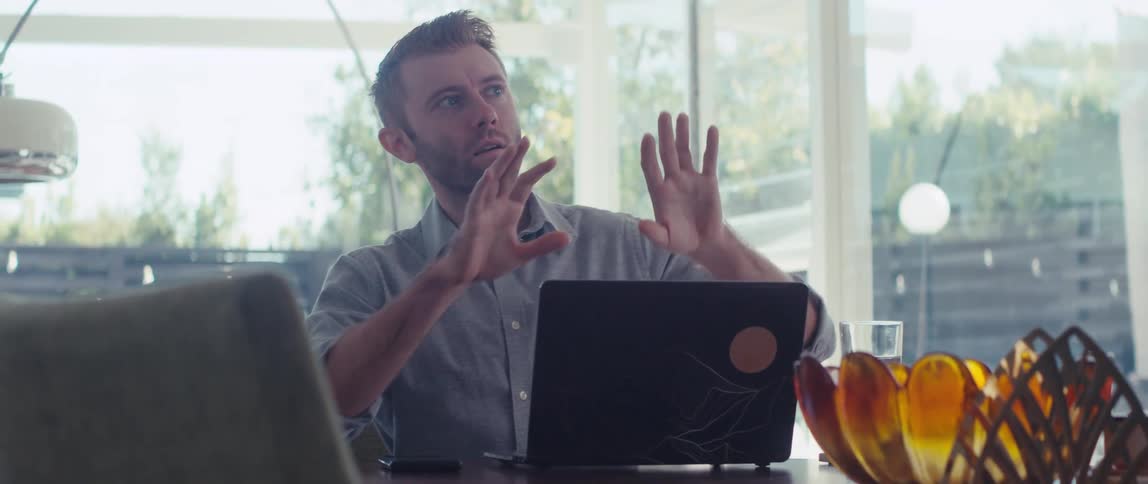 A man in a shirt having a meeting on his laptop in a welllit living room in a modern home