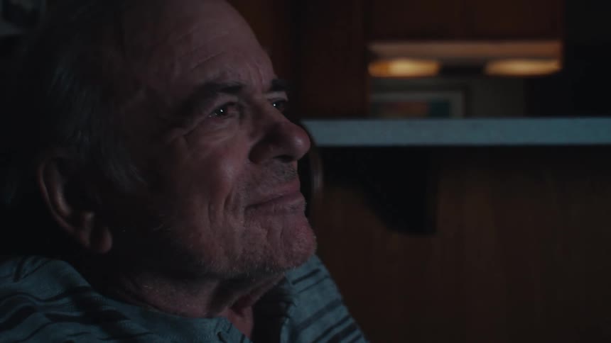 The face of an elderly man who is sitting looking straight ahead and where there is a glow coming towards his face