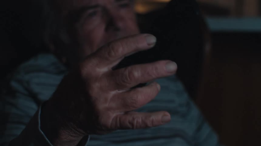 Portrait of an elderly man sitting holding a television remote control