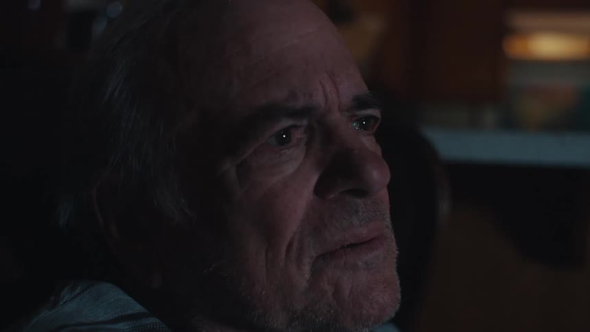 A man is sitting at home watching television in a dark room